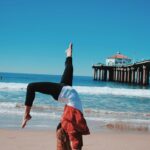 매일 15분, 맨몸 운동으로 건강과 탄탄한 체력을! woman wearing red jacket and black leggings doing hand stand in seashore